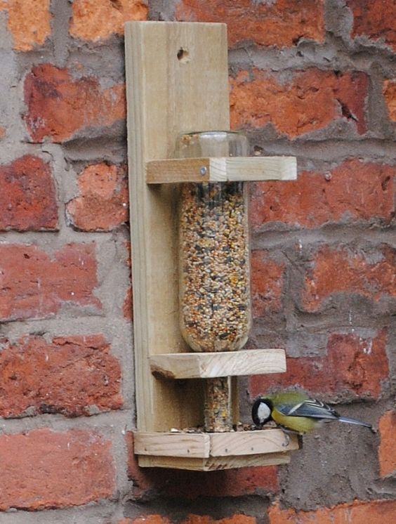 Support en bois avec bouteille en verre pour stocker les graines pour oiseaux.