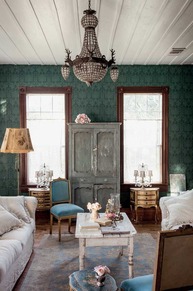 Une décoration typiquement Shabby Chic est réalisée ainsi: sobriété et élégance présentes dans le vert foncé du mur, dans le lustre et dans le bois contrastées par l'aspect vieilli du placard et de la table basse 