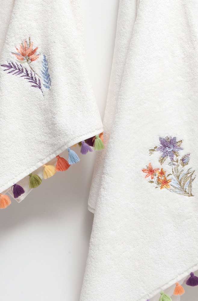Super délicate, cette serviette blanche a reçu une petite broderie fleurie complétée par la bordure de franges colorées
